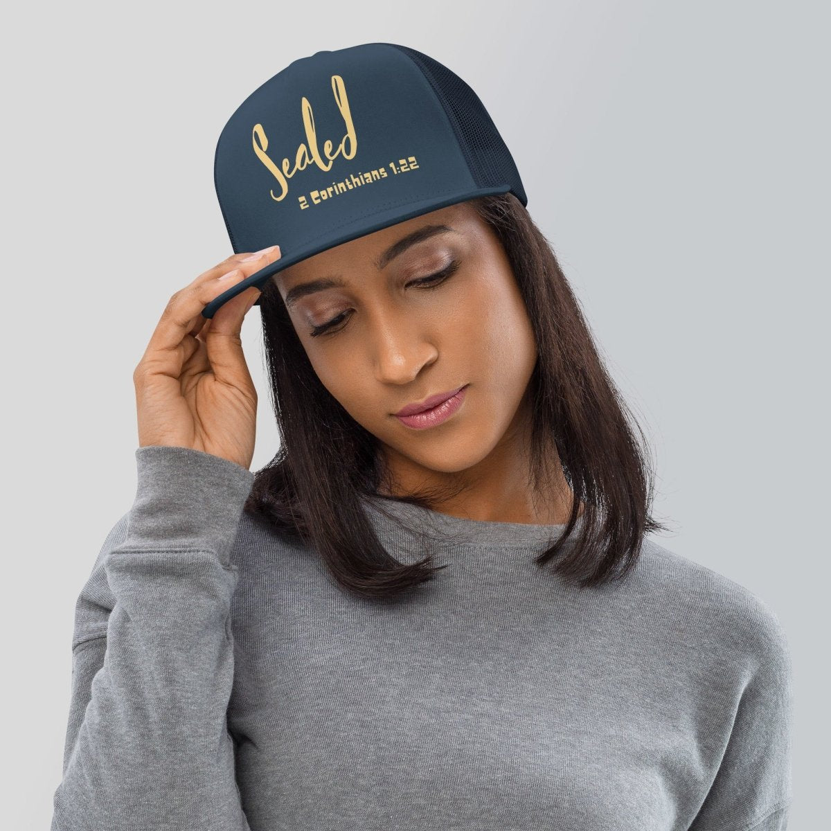 Woman wearing a navy blue trucker hat with gold text Sealed 2 Corinthians 1:22